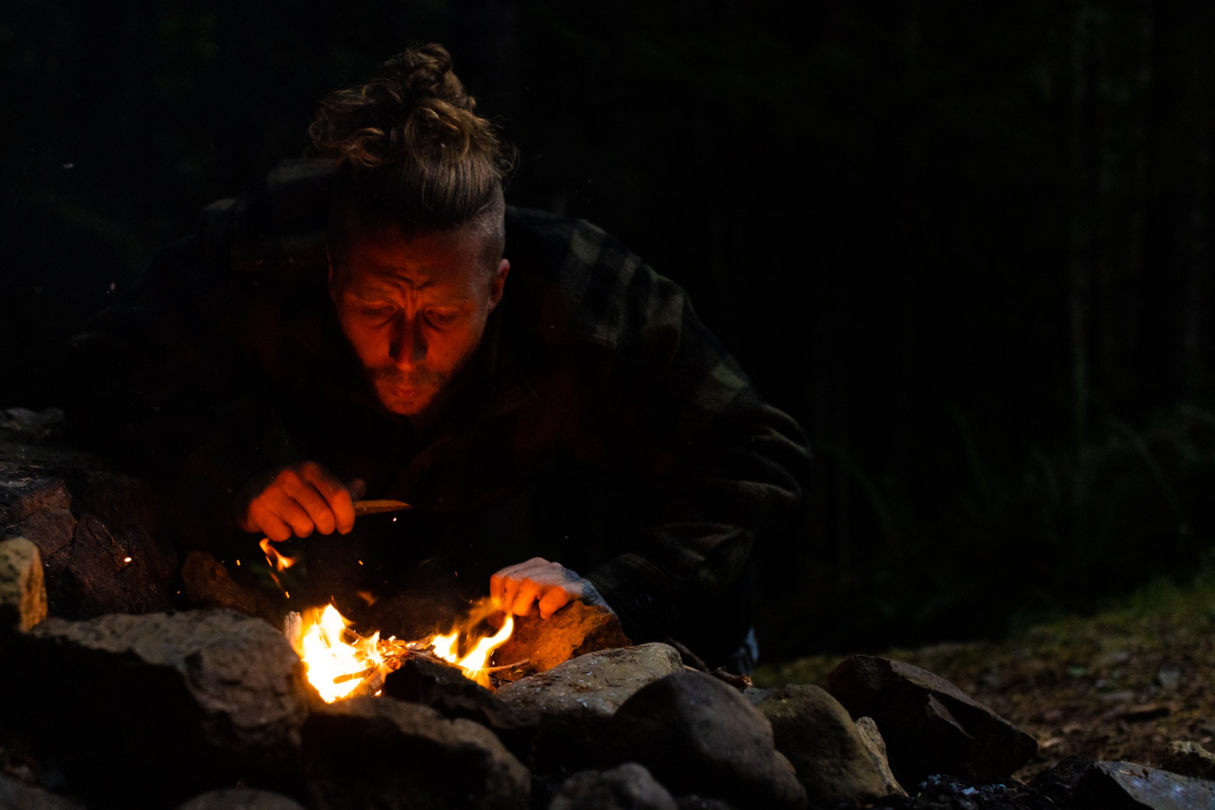 Evan Meyer blowing on a campfire at night